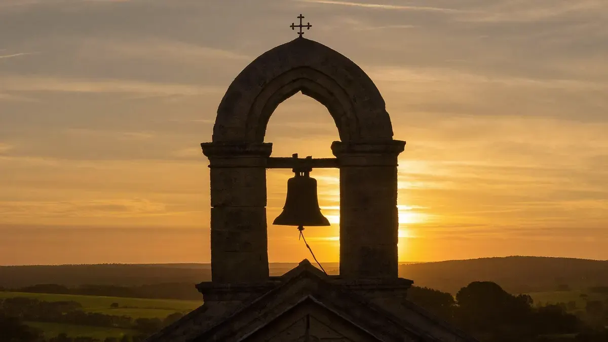 Torre de igreja antiga com sino ao entardecer, céu dourado