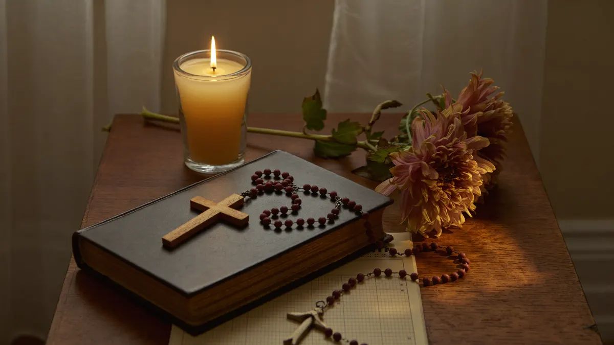 Mesa de oração com vela acesa, terço, Bíblia fechada e calendário marcando a véspera de Todos os Santos