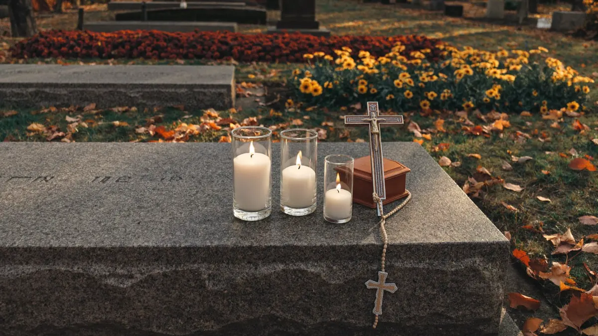 Velas acesas e terço sobre uma lápide simples em um cemitério ao entardecer, em clima de oração pelos falecidos