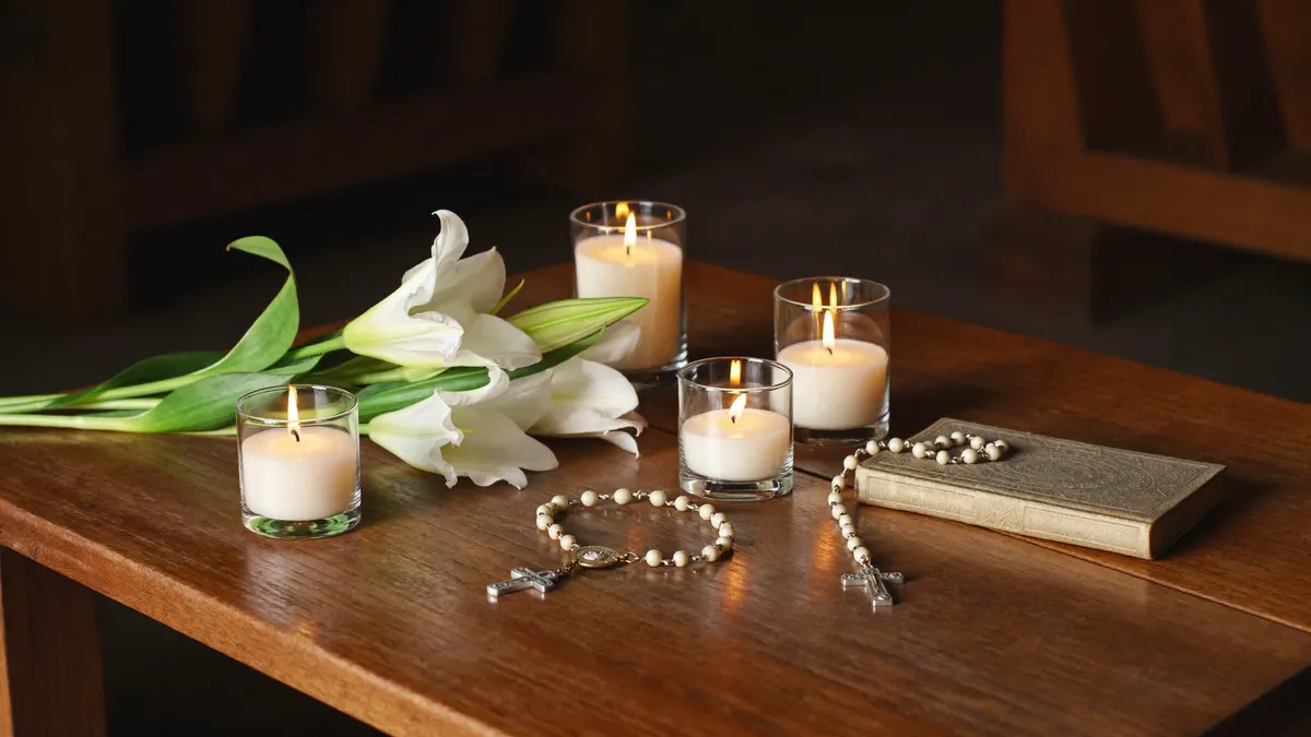 Velas acesas, terço e flores brancas sobre uma mesa de oração em memória dos fiéis falecidos